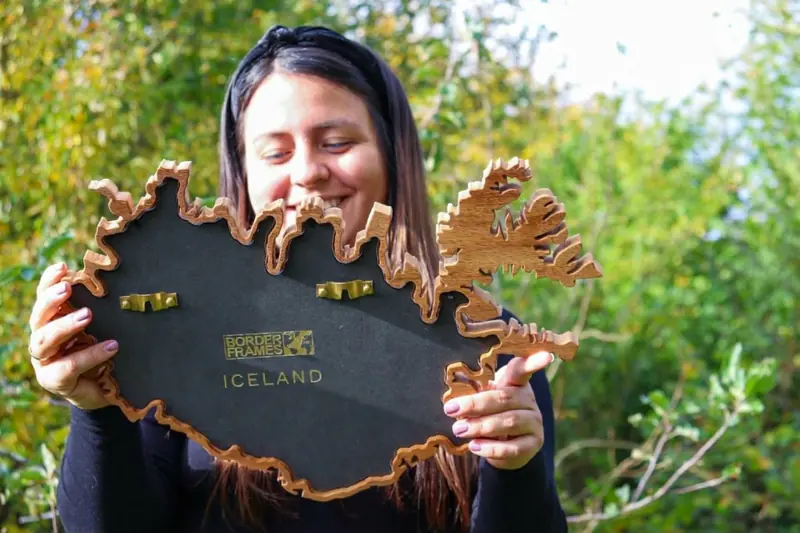 Macarena smiling at her Iceland Borderframe, holding it up to show the engraved backplate and brass hangers